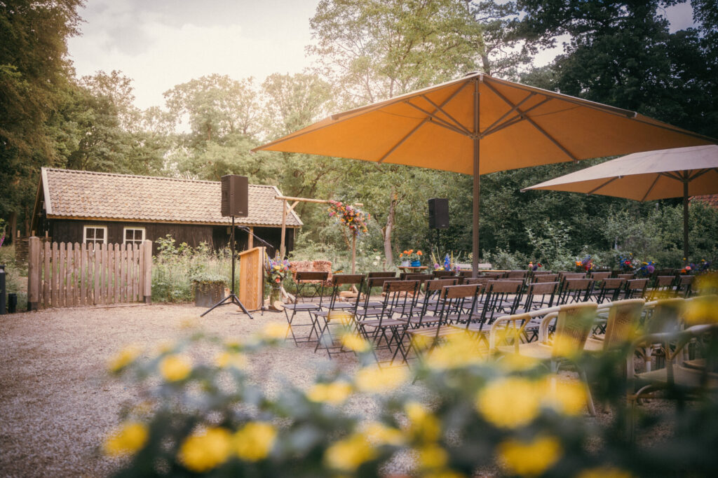 Buitenlocatie voor een bruiloft met parasols, tafels en bloemen in de tuin
