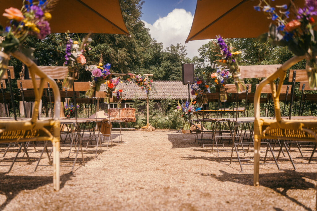 Ceremonieopstelling in de buitenlucht met stoelen en bloemenbogen